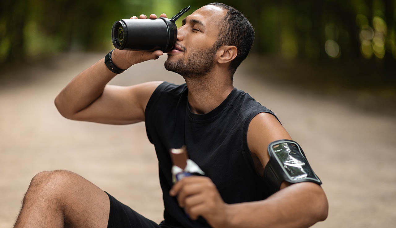 Hombre tomando batido de proteínas y barrita