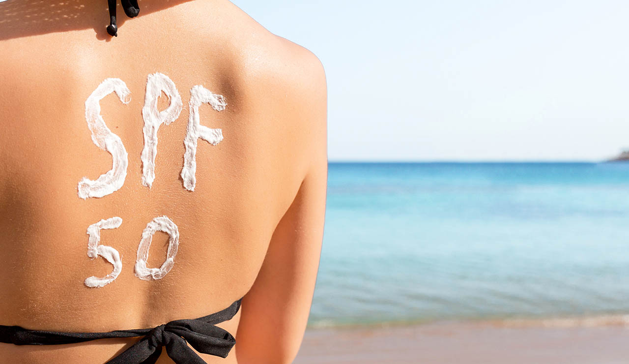mujer en la playa con crema solar en la espalda