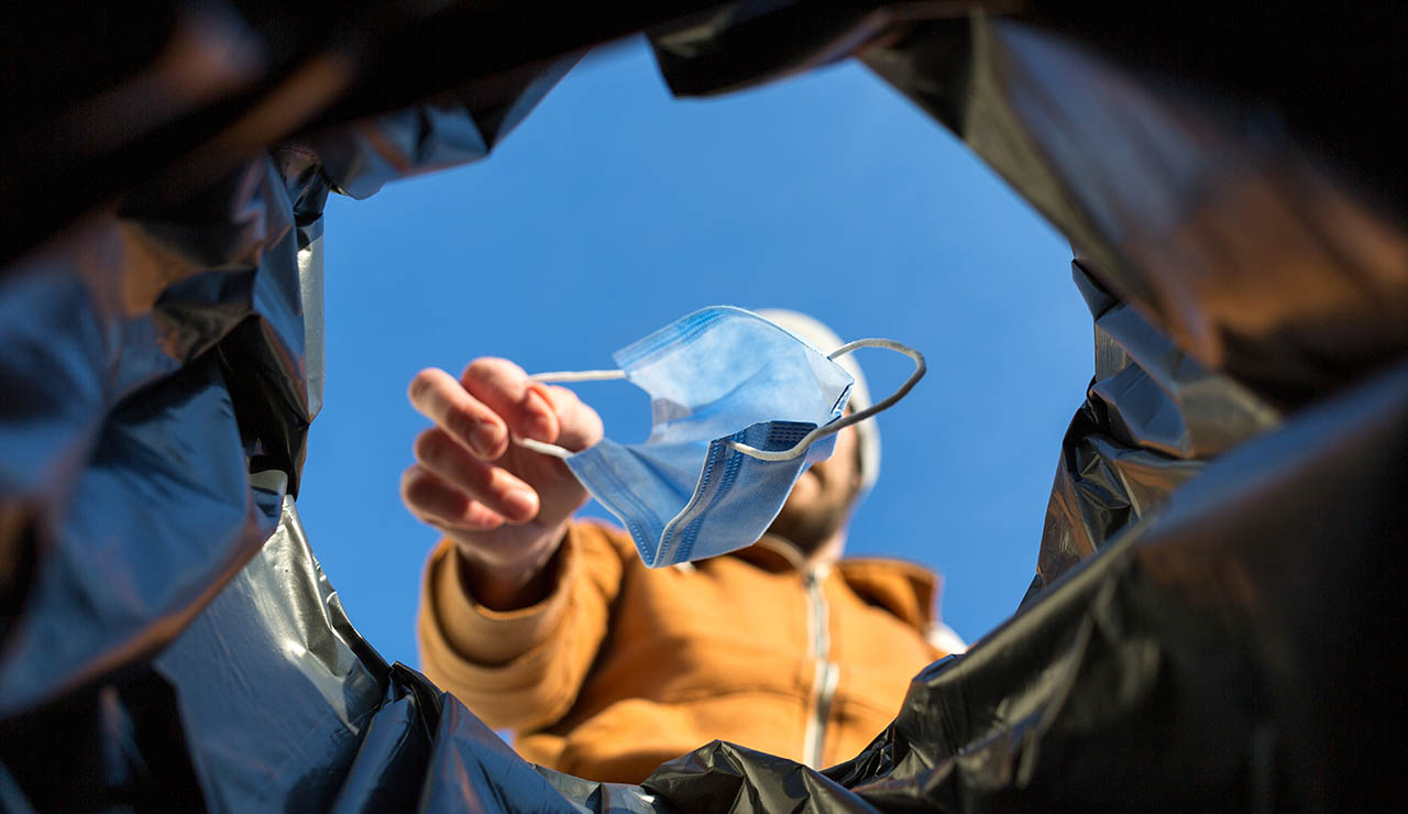 Persona tirando una mascarilla a la basura