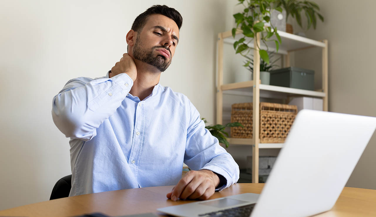 Hombre teletrabajando con dolor en el cuello