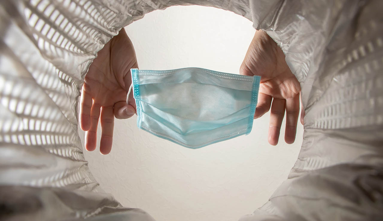 manos tirando una mascarilla a la basura